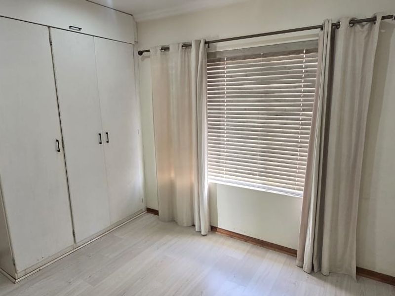 A bright, empty bedroom featuring built-in wardrobes, light laminate flooring, and venetian blinds, offering a clean canvas for personalization.