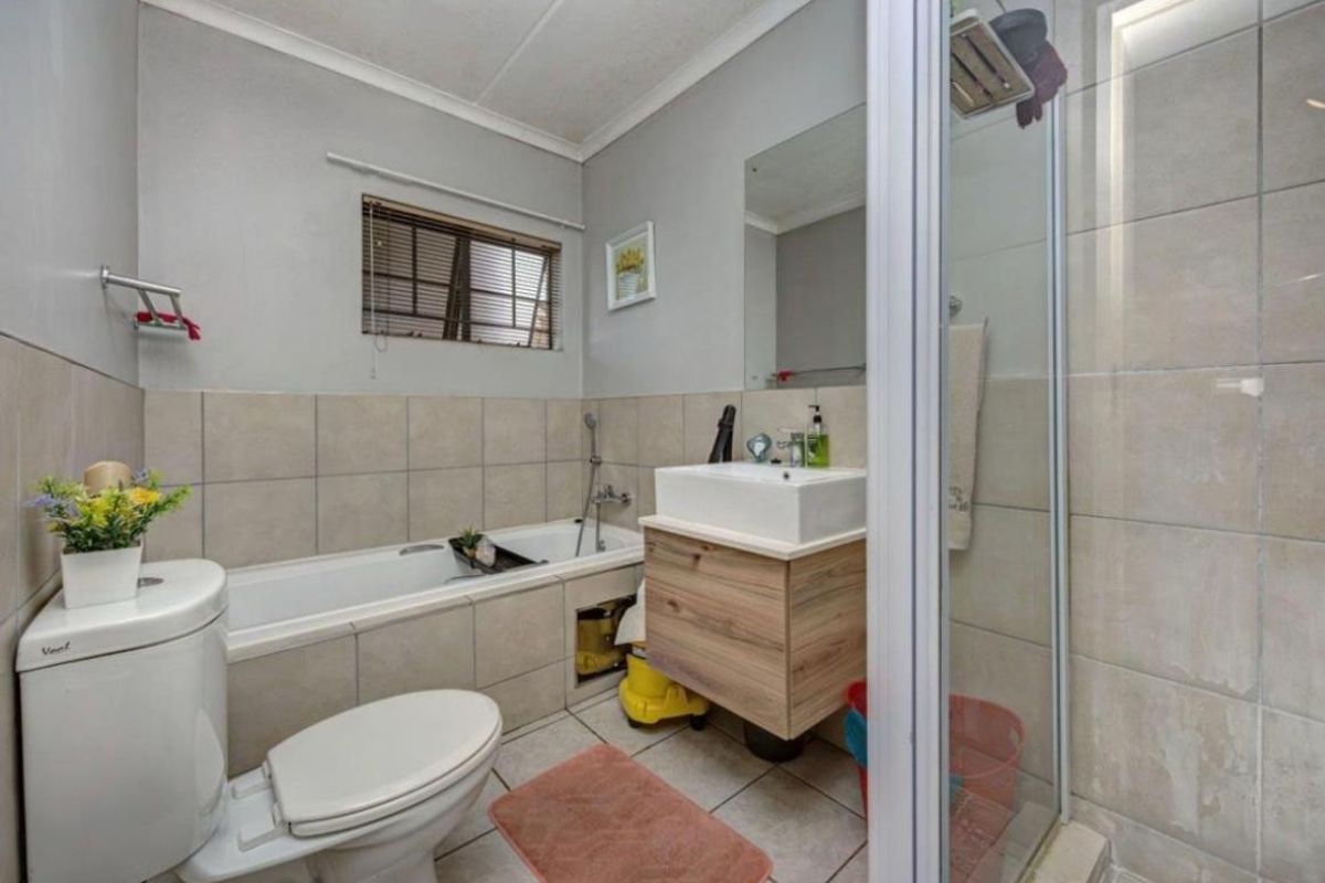 A functional bathroom featuring a built-in bathtub, separate shower enclosure, vanity cabinet with basin, and neutral ceramic tiling throughout.