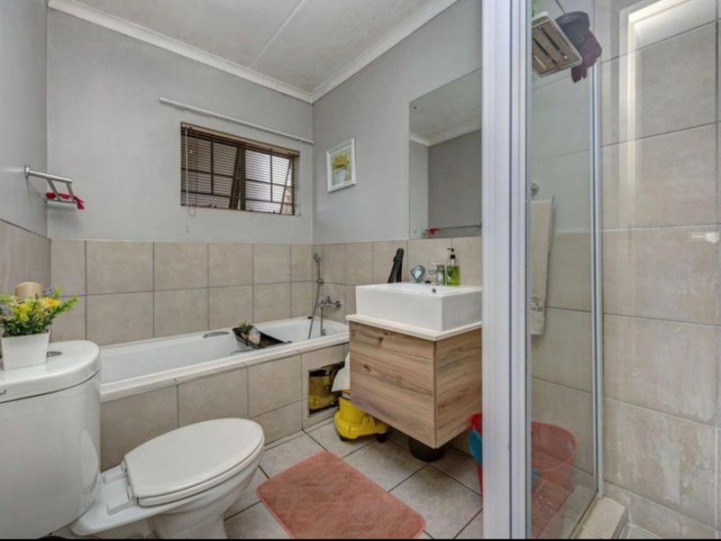 A functional bathroom featuring a built-in bathtub, separate shower enclosure, vanity cabinet with basin, and neutral ceramic tiling throughout.