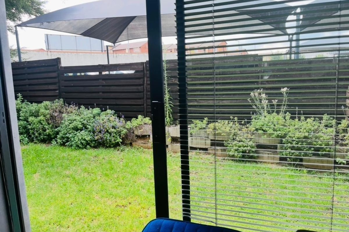 A view from inside looking out onto a private rear garden featuring a lawn, timber fencing, and a shade sail structure.
