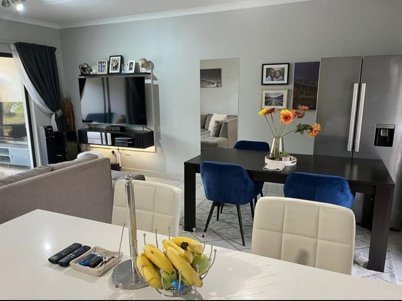 An open-plan living and dining area featuring tiled flooring, neutral wall tones, and a wall-mounted mirror, creating a functional and cohesive living space.