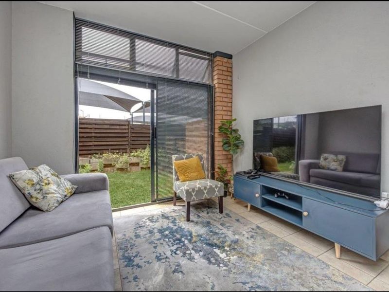 A bright living room featuring tiled flooring, an exposed brick accent column, and a large sliding glass door providing direct access to the garden.