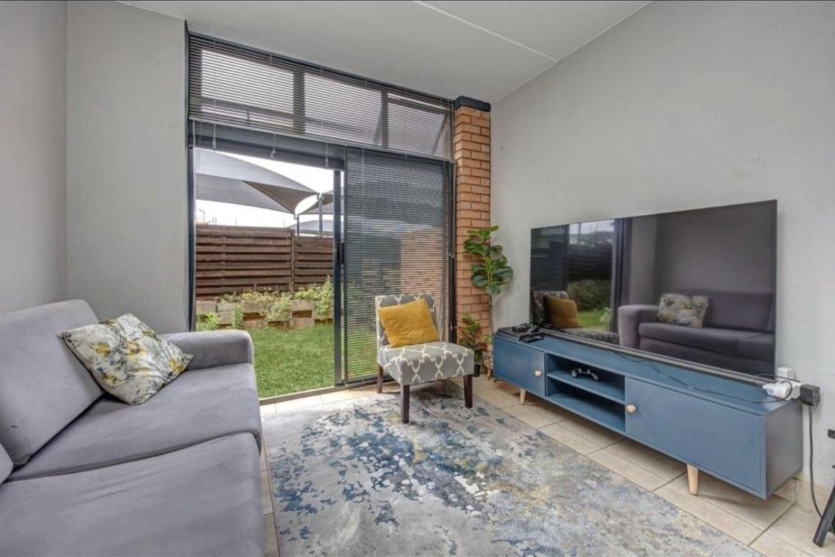 A bright living room featuring tiled flooring, an exposed brick accent column, and a large sliding glass door providing direct access to the garden.