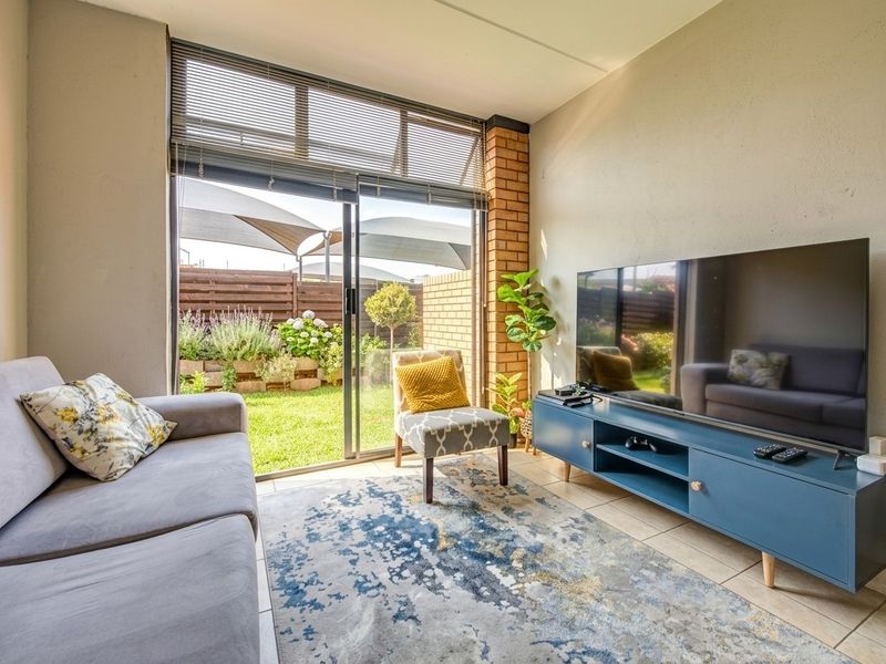 A bright living room featuring tiled flooring, an exposed brick accent pillar, and a large sliding glass door providing direct access to the garden.
