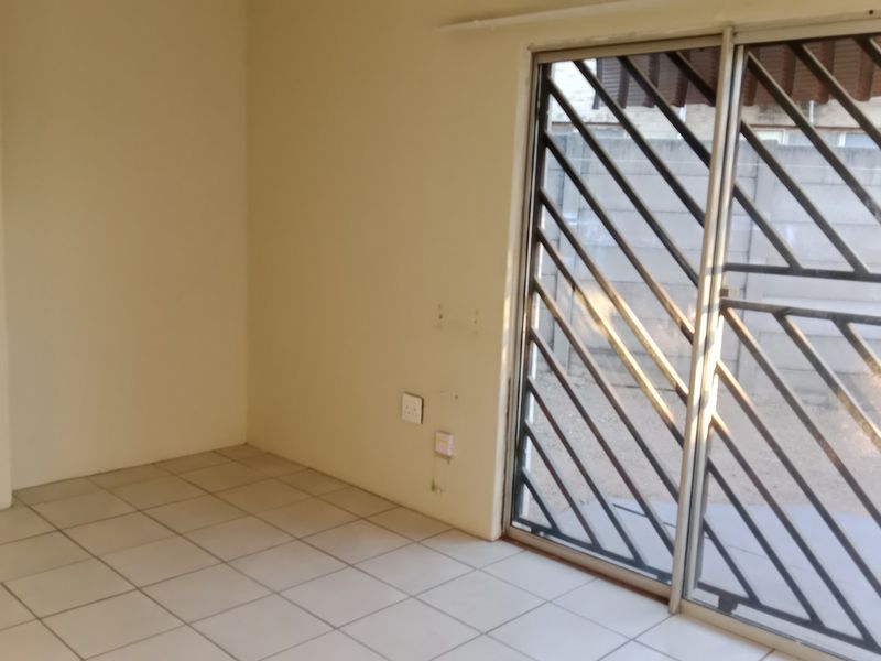 An empty living area featuring tiled flooring and a sliding glass door with an integrated security gate, providing access to the exterior.