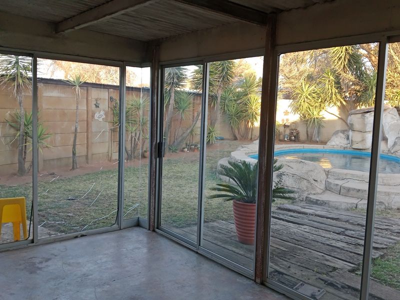 Enclosed patio area featuring large sliding glass doors with views of the garden and swimming pool, requiring maintenance and cosmetic updates.
