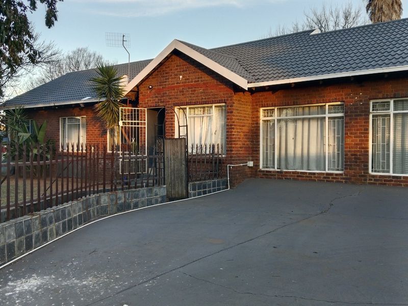 Front elevation of a face brick house featuring a tiled roof, paved driveway, and secure metal fencing with security gates.