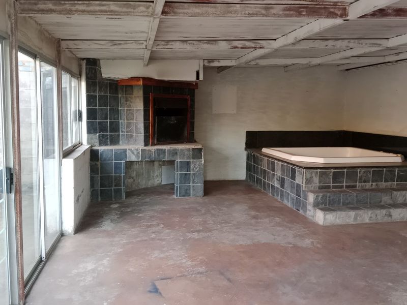 Enclosed patio area featuring a built-in braai, a tiled spa bath, and sliding glass doors, offering potential for a versatile entertainment space.