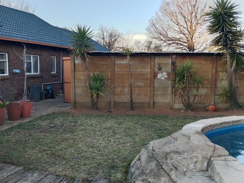 Rear garden area featuring a swimming pool with rock-style coping, a brick exterior wall, and a precast concrete boundary fence.