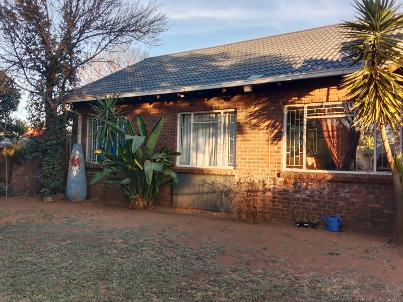 A view of the rear face brick facade featuring a tiled roof and security bars on the windows, set against a garden area.