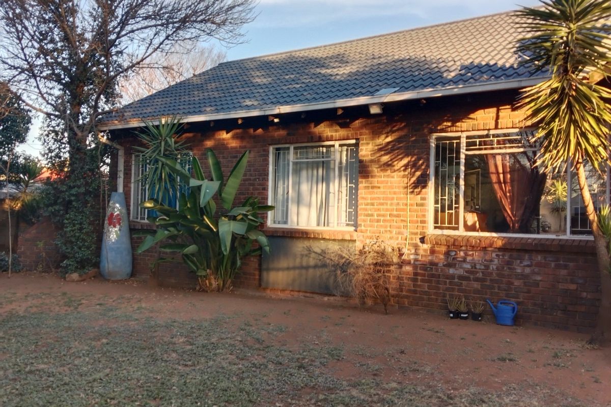 A view of the rear face brick facade featuring a tiled roof and security bars on the windows, set against a garden area.