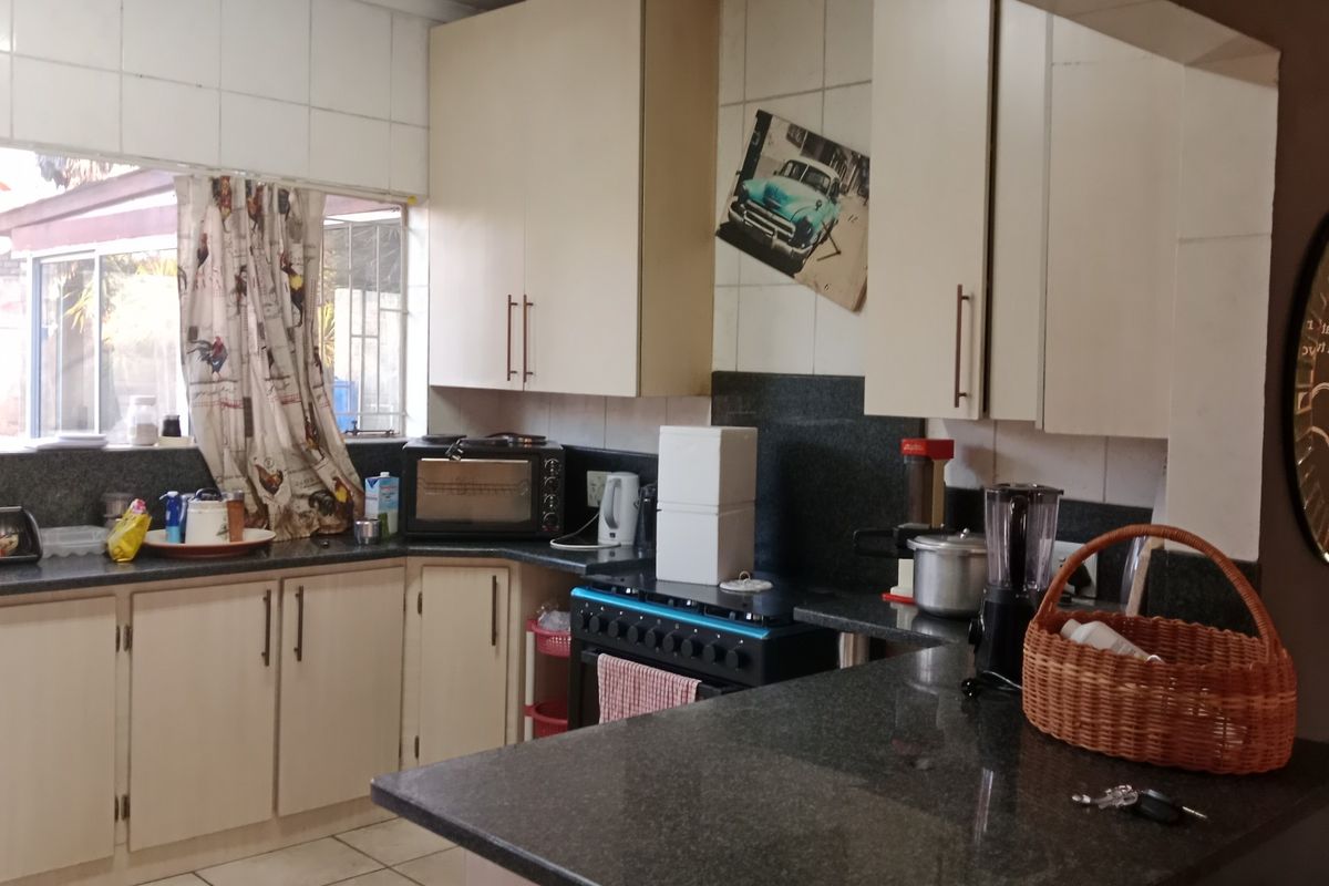 A functional kitchen featuring granite countertops, built-in cabinetry, a gas stove, and tiled finishes, offering a practical layout with potential for modern updates.