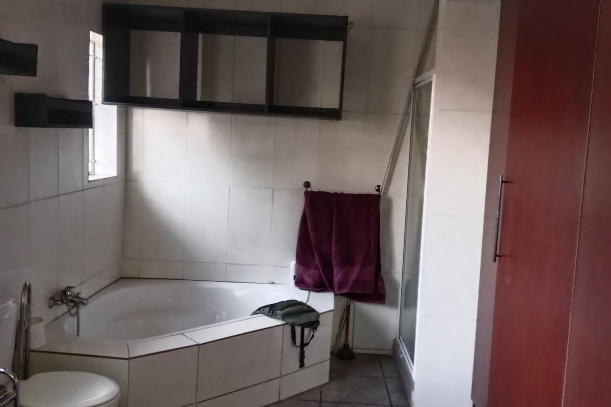 A functional bathroom featuring a corner bathtub, separate shower enclosure, and built-in cabinetry, offering potential for a modern renovation.