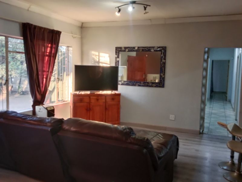 A living room featuring laminate flooring, track lighting, and large windows with security bars, providing access to an adjacent hallway.