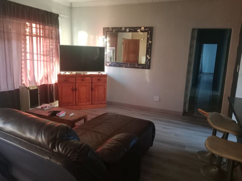 A living room area featuring laminate flooring and access to a hallway, providing a functional space for relaxation.