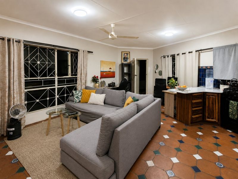 Open-plan living and kitchen area featuring terracotta tiled flooring, ceiling fan, and functional kitchen cabinetry with security bars on windows.
