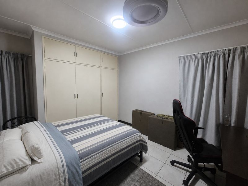 A functional bedroom featuring built-in cupboards, tiled flooring, and neutral wall finishes, providing a practical space for rest or study.
