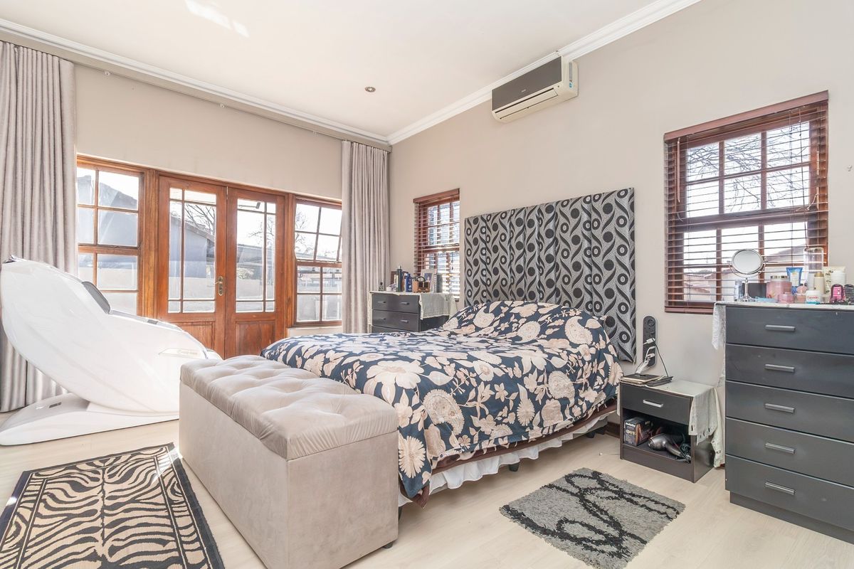 A well-lit bedroom featuring laminate flooring, a wall-mounted air conditioning unit, and wooden framed glass doors providing access to the exterior.