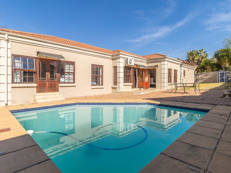 Rear exterior view of the property featuring a swimming pool, paved patio area, and direct access to the home via timber-framed doors.