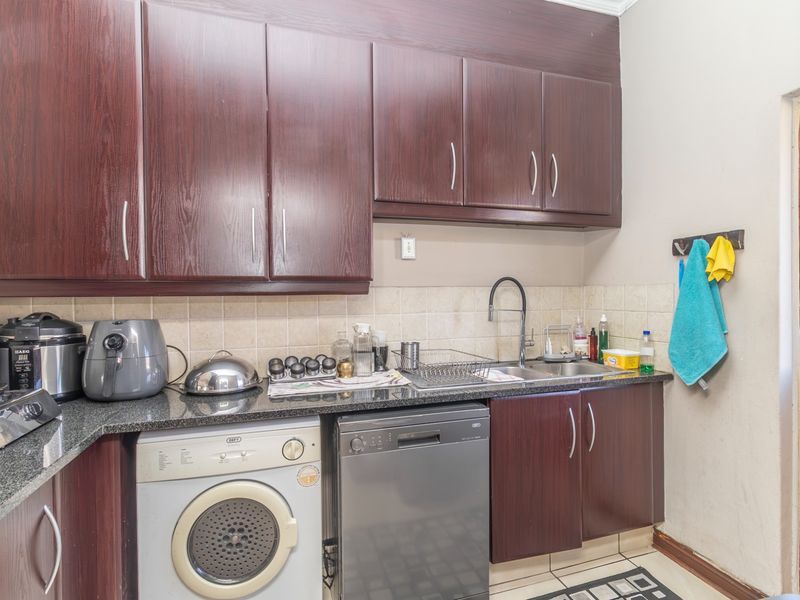 A functional scullery featuring dark wood cabinetry, granite countertops, a stainless steel double sink, and integrated space for a dishwasher and laundry appliance.
