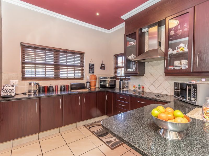 A well-maintained kitchen featuring dark wood cabinetry, granite countertops, a tiled backsplash, and a distinctive red ceiling with crown molding.