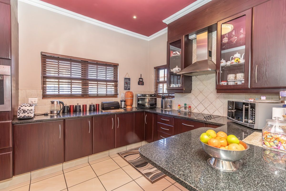 A well-maintained kitchen featuring dark wood cabinetry, granite countertops, a tiled backsplash, and a distinctive red ceiling with crown molding.