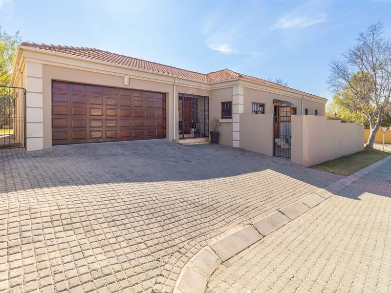 Front exterior view of a well-maintained house featuring a paved driveway, double garage, and secure boundary wall with gated entrance.