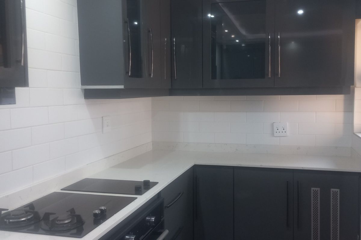 Modern kitchen featuring dark grey cabinetry, white stone countertops, and a clean white subway tile backsplash with integrated cooking appliances.