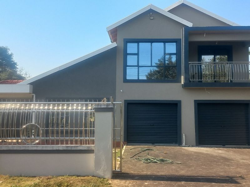 Modern double-story residential home featuring a double garage, upper-level balcony with stainless steel railing, and a secure perimeter wall.
