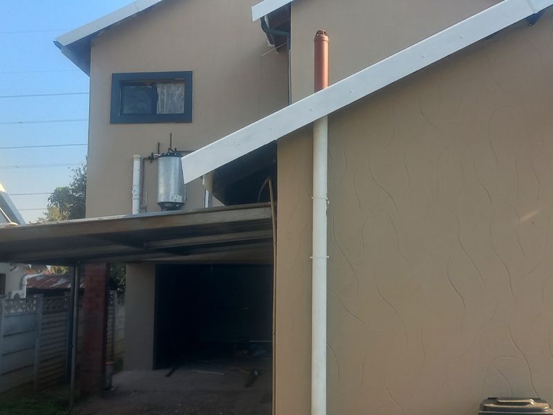 Rear view of the property featuring a carport structure, external geyser, and textured exterior wall finish.