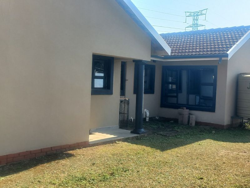 Rear view of the house featuring plastered walls, dark aluminium window frames, a covered patio area, and an installed water tank on the property.