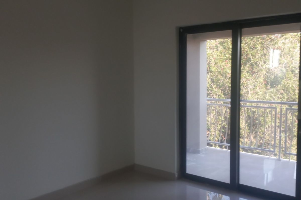 An empty bedroom featuring neutral tiled flooring and a large sliding glass door providing access to an outdoor balcony.