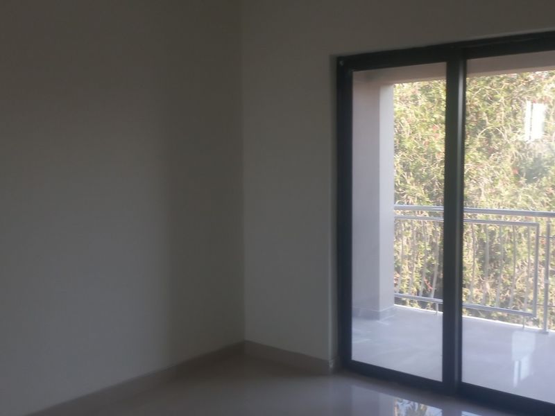 An empty bedroom featuring neutral tiled flooring and a large sliding glass door providing access to an outdoor balcony.