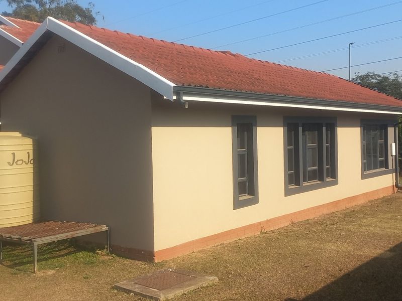 Rear view of the house featuring a tiled roof, rainwater storage tank, and surrounding garden area with perimeter walling.