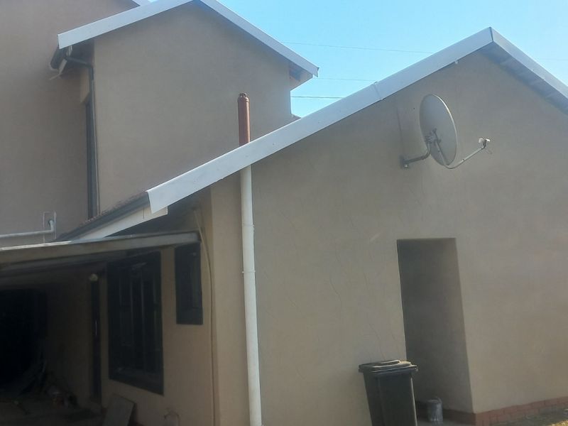 Rear view of the house featuring plastered walls, a tiled roof, an external geyser unit, and a covered patio area.