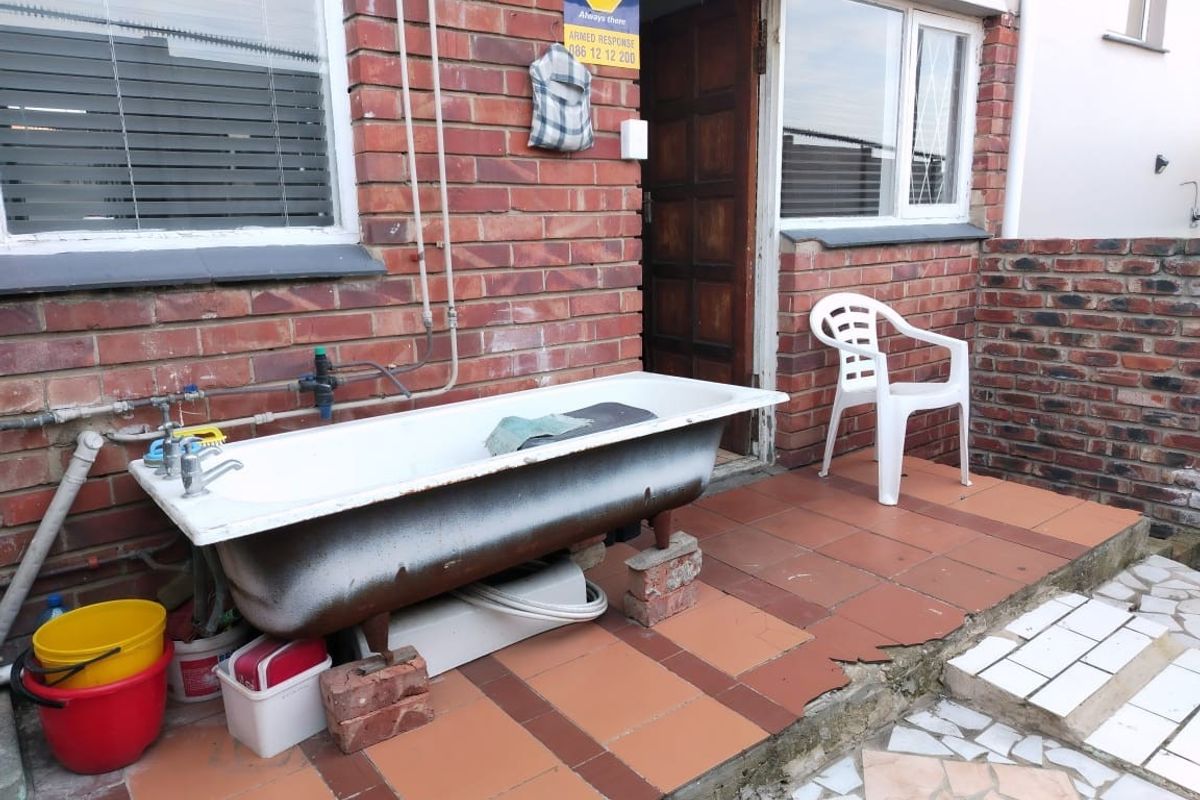 Rear exterior area featuring exposed brickwork, tiled patio flooring, and security features, currently utilized for external utility purposes.