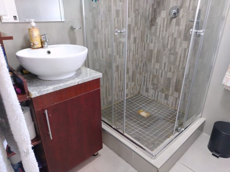 A functional bathroom featuring a vessel sink on a vanity cabinet and a glass-enclosed shower with textured wall tiling.