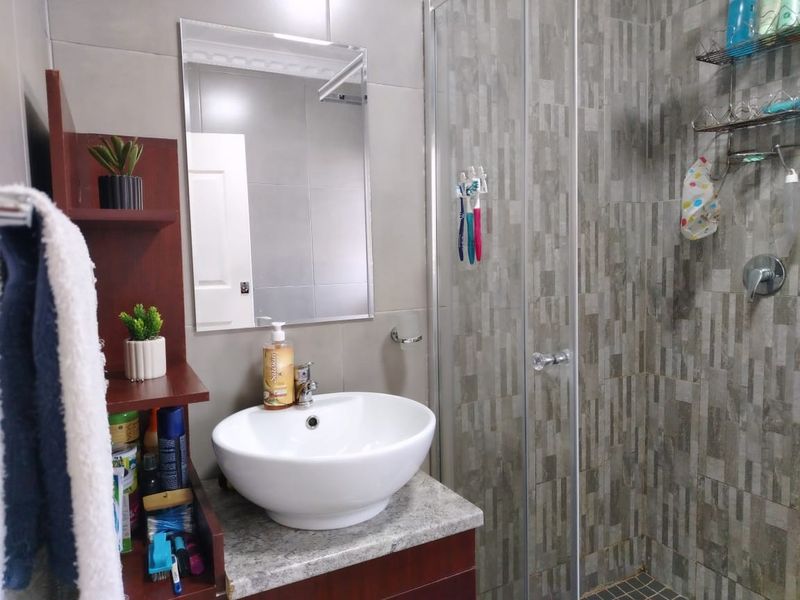 A modern bathroom featuring a vessel sink on a stone vanity, a wall mirror, and a glass-enclosed shower with textured wall tiling.