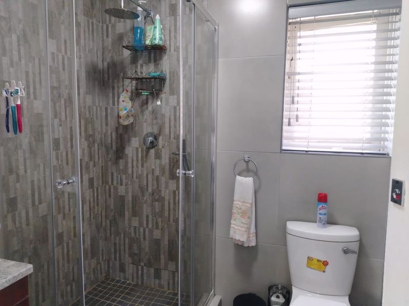 A modern bathroom featuring a glass-enclosed shower with a rain shower head, textured wall tiling, and a standard toilet.