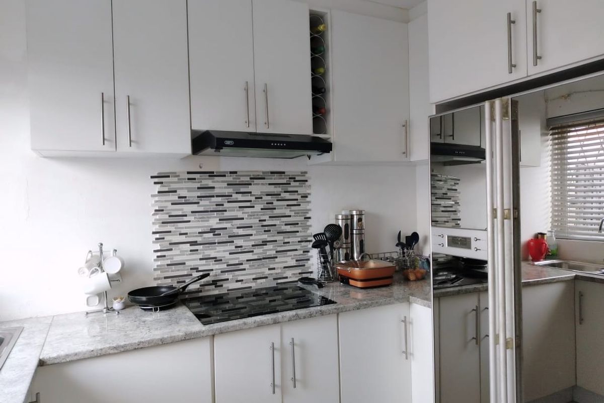 A functional kitchen featuring white cabinetry, granite countertops, a mosaic tile backsplash, and an integrated hob with an extractor fan.
