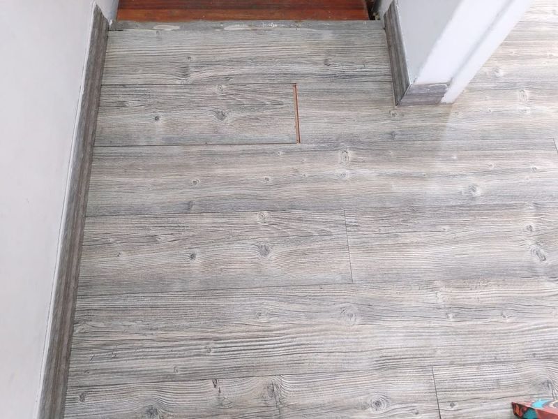 A close-up view of a hallway floor featuring wood-look laminate planks with visible installation gaps and damage.