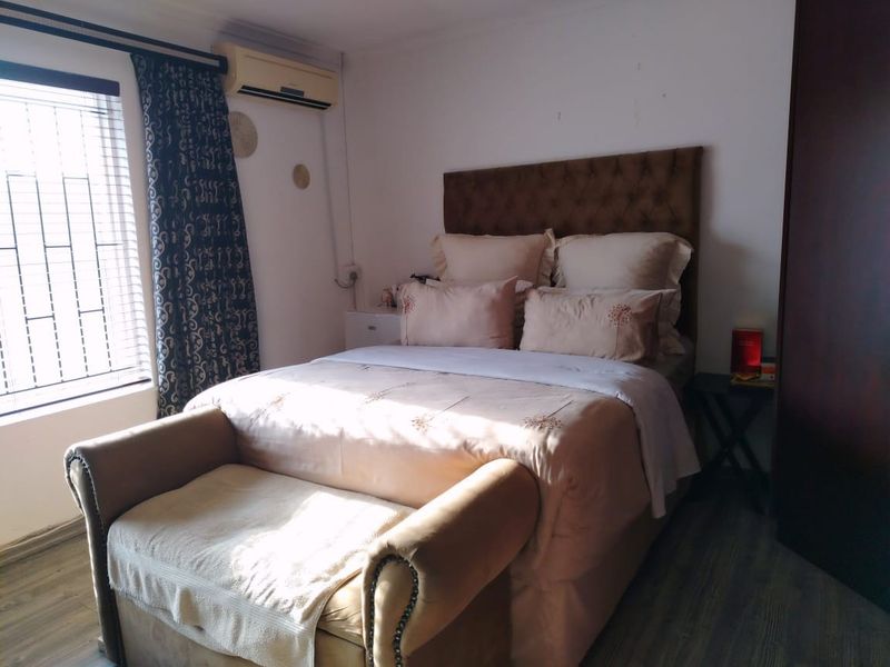 A functional bedroom featuring laminate flooring, a wall-mounted air conditioning unit, and security bars on the window.