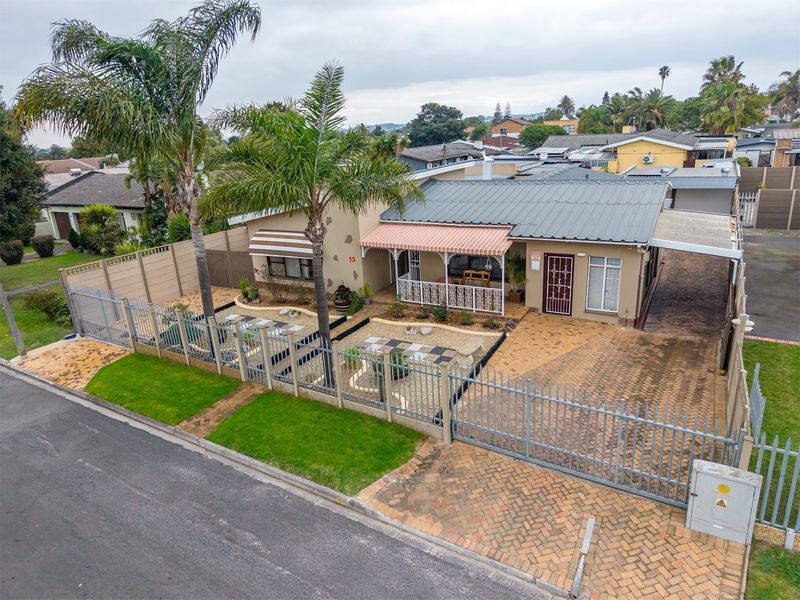 Elevated view of the front facade featuring a paved driveway, steel security fencing, covered patio area, and a metal roof.