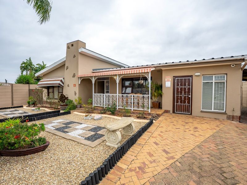 Front elevation of a single-story house featuring a brick-paved driveway, covered patio with decorative trim, and low-maintenance landscaped garden area.