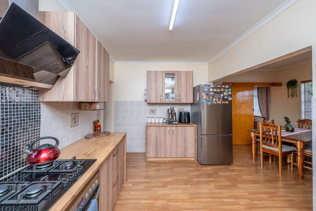 Functional kitchen featuring wood-look cabinetry, gas hob, built-in oven, extractor fan, and mosaic tile backsplash, flowing into an adjacent dining area.