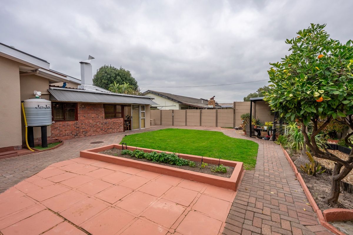 A well-maintained rear garden featuring a paved patio, raised garden bed, lawn area, and a brick-walled exterior with a water tank.