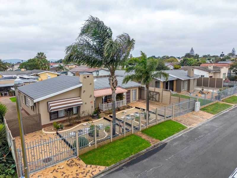 Aerial view of a residential property featuring a metal roof, paved driveway, perimeter fencing, and a well-maintained front garden area.