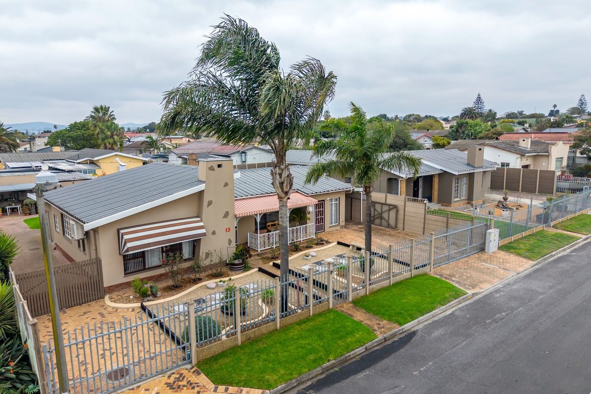 Aerial view of a residential property featuring a metal roof, paved driveway, perimeter fencing, and a well-maintained front garden area.