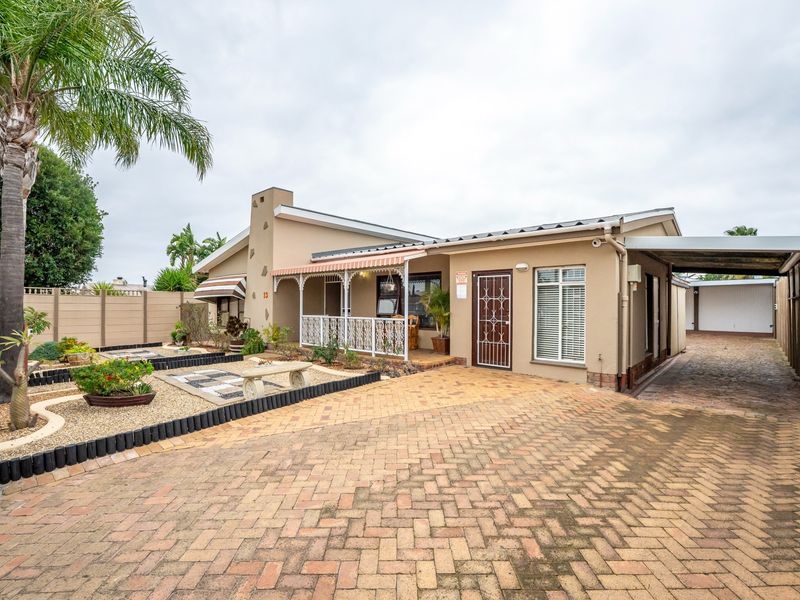 Front elevation of a single-story residence featuring a brick-paved driveway, carport, covered patio area, and established low-maintenance garden.