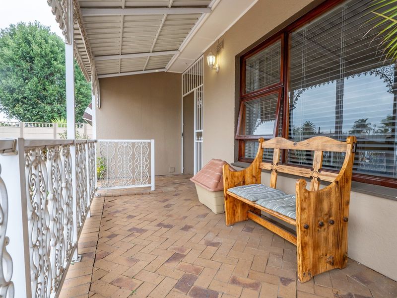 A covered patio area featuring paved flooring, a decorative wrought iron balustrade, and a secure entrance door with a security gate.